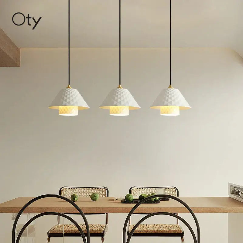 Three white textured ceramic pendant lights with gold accents hang above a kitchen dining table