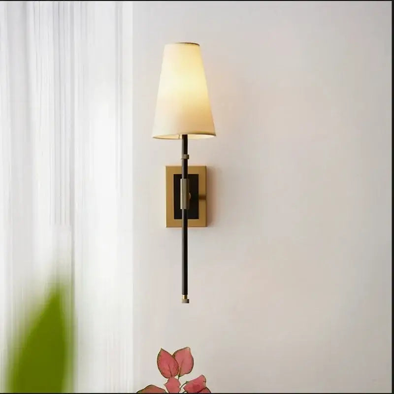 A sleek black wall lamp with a warm cream copper cloth led shade and square brass backplate for bedroom use