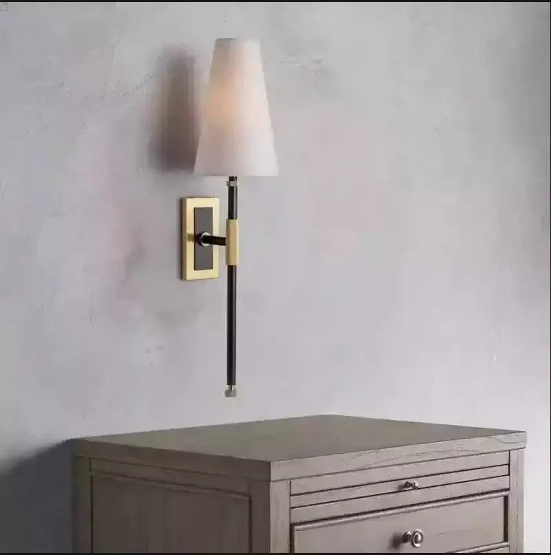 A sleek black and brass wall lamp with a copper cloth led tapered white fabric shade for bedroom use