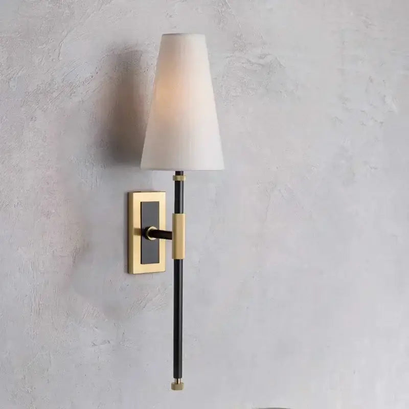 A sleek black and brass wall lamp with a cream copper cloth led fabric shade for bedroom lighting