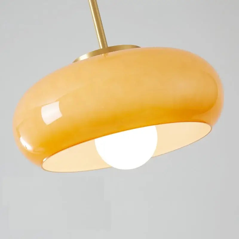A sleek amber copper pendant light with a rounded glass dome and brass-finished metal stem by DecorBites
