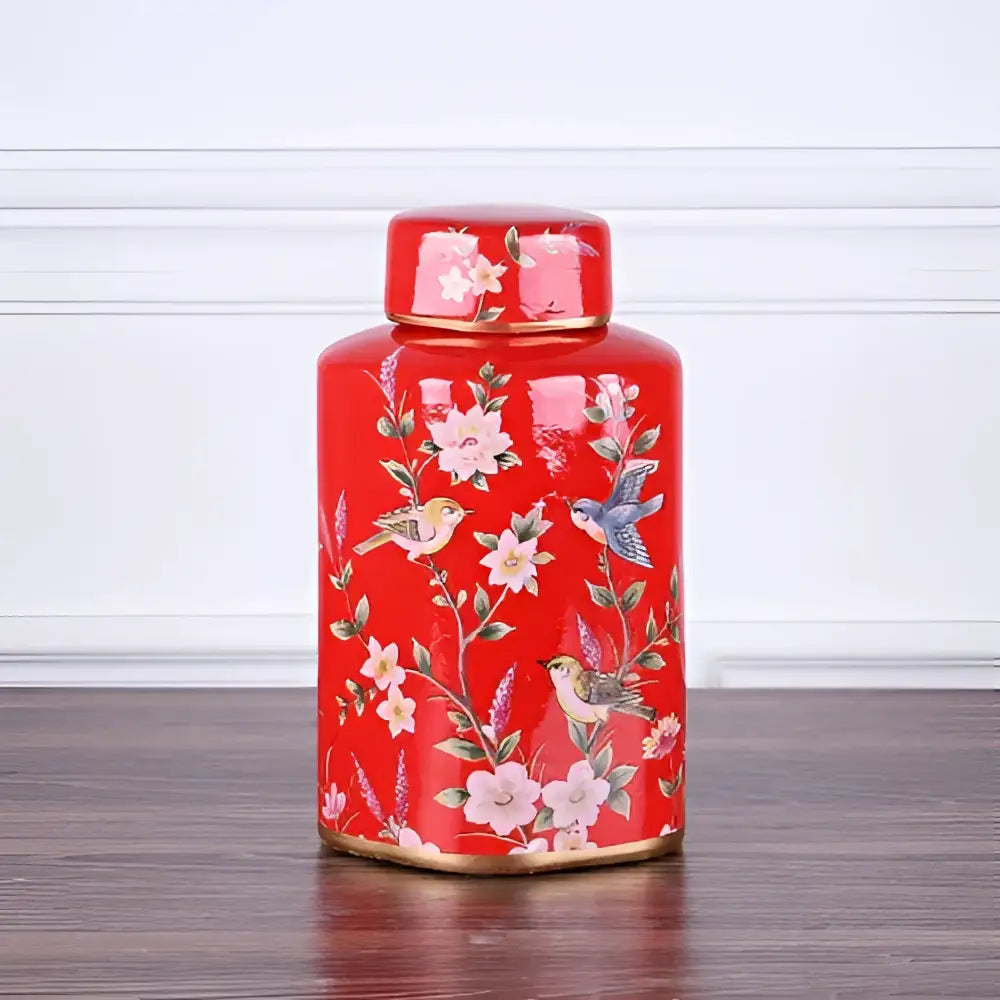 A vibrant red decorbites country ceramic tea canister with floral and bird motifs and gold-trimmed lid and base