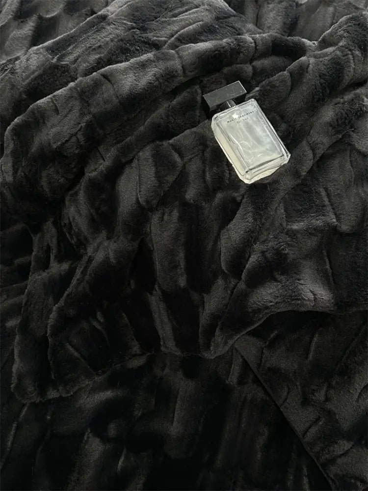 A sleek glass perfume bottle with a black cap resting on decorbites cozy faux rabbit fur bedding set in black and grey