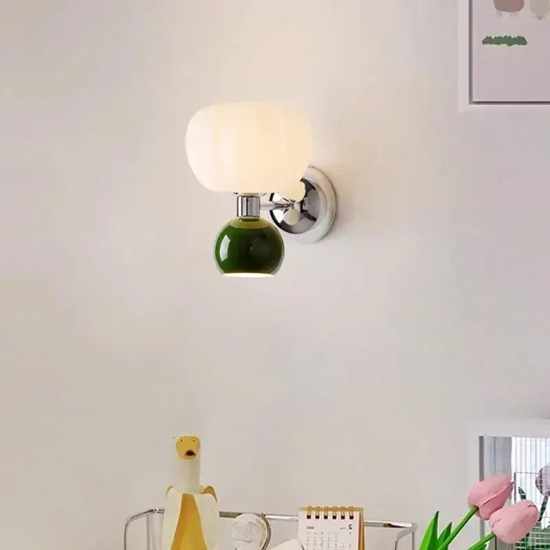 A modern decorbites cream breeze frosted glass pumpkin wall sconce with a green ceramic base and chrome bracket