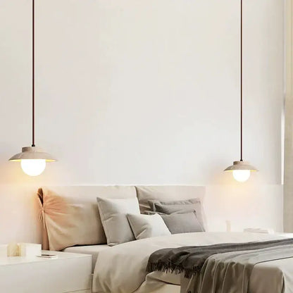 Two minimalist decorbites cream stone pendant lamps with warm bulbs and matte beige shades hang above a bed