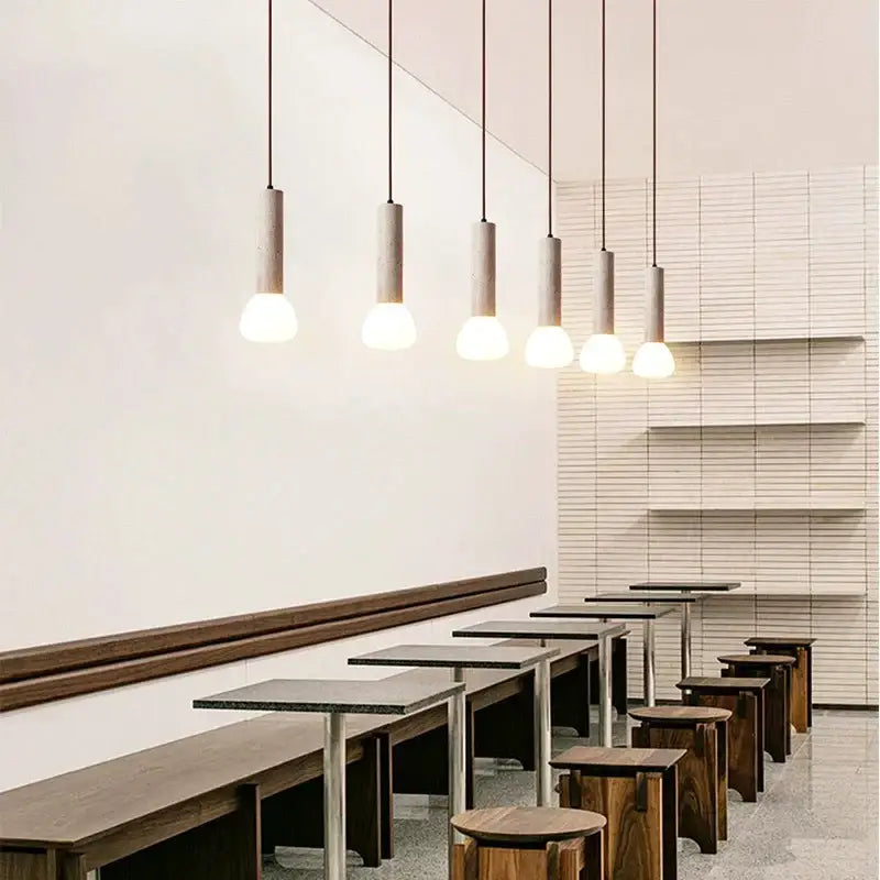 Six cream style cylindrical concrete pendant lamps with warm white bulbs by decorbites cream style in a modern café setting