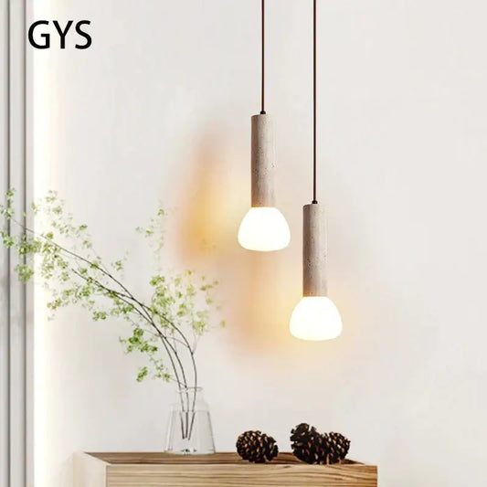 Two minimalist decorbites cream style concrete pendant lamps with warm spherical bulbs hang from dark cords