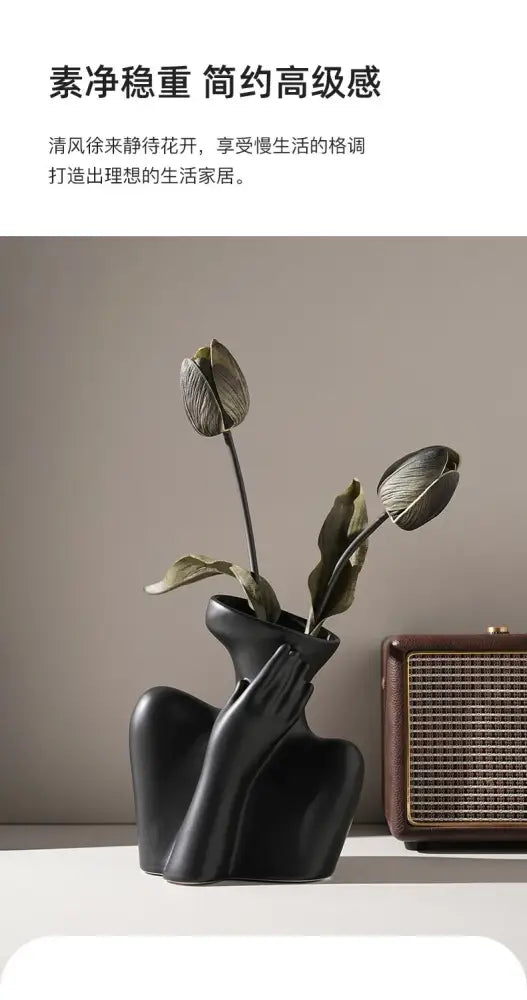 Black ceramic human vase shaped like a woman’s torso with hand cupping cheek holding dried tulips for home decor