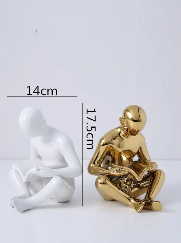 Golden metallic decorbites creative ceramics sculpture of a seated person reading with smooth contours and reflective surface