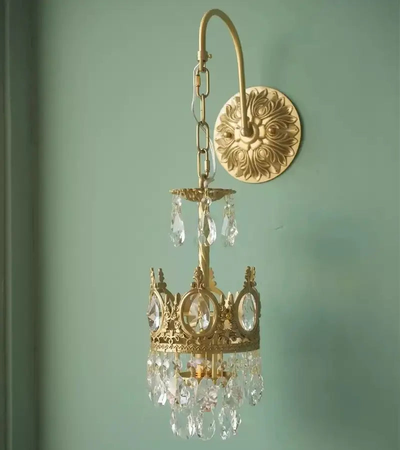 Gold-toned decorbites crown crystal chandelier wall sconce with clear crystal droplets and ornate filigree detailing