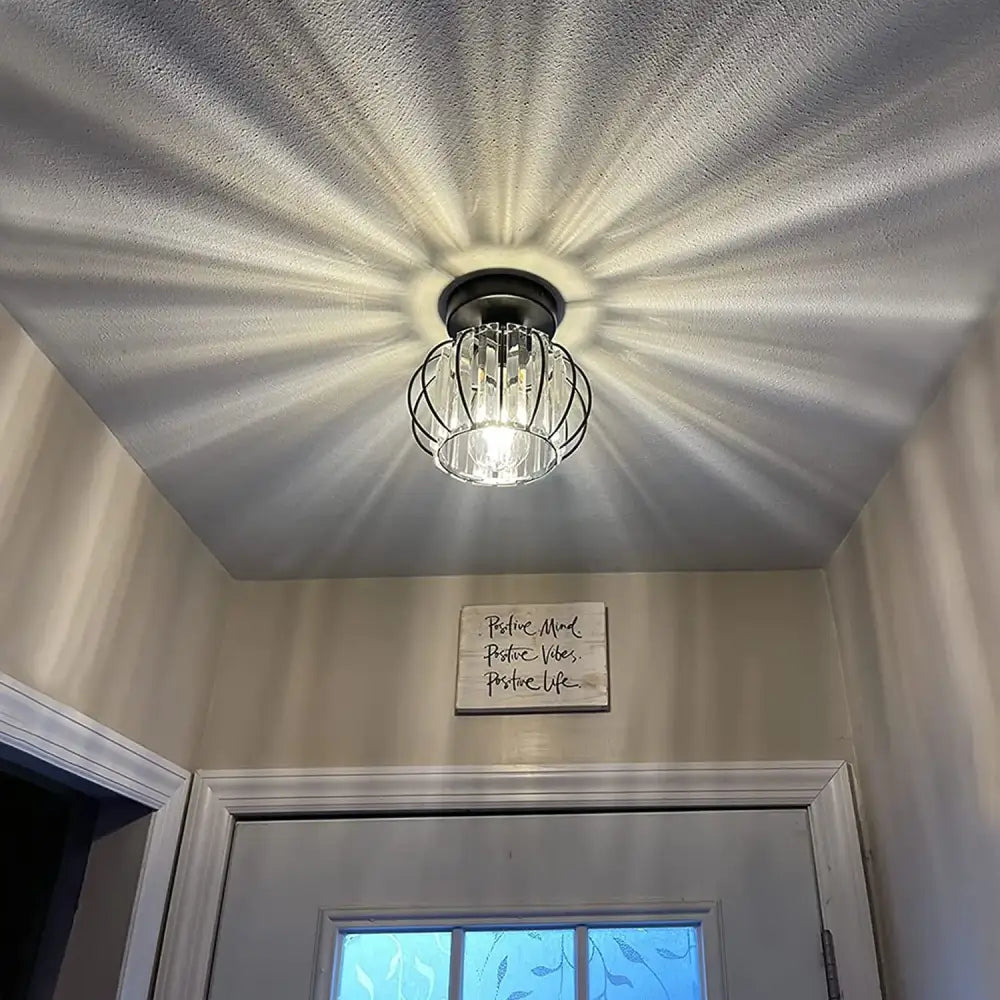 DecorBites™ crystal ceiling light fixture with black metal cage and clear glass panels emitting warm white light