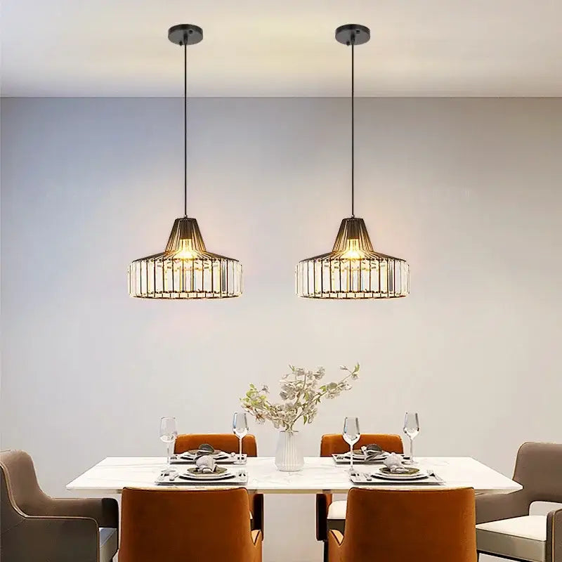 Two black and gold decorbites crystal chandelier pendant lights with crystal accents hang above a dining table