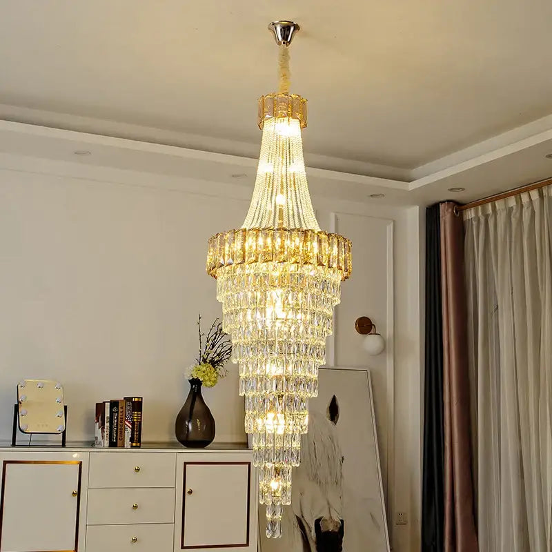 A multi-tiered gold-toned decorbites crystal chandelier with hanging crystals emitting warm light for luxury spaces