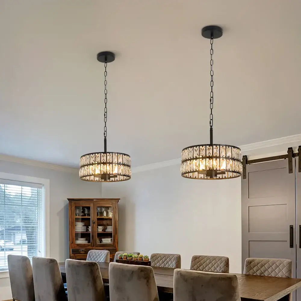 Two black chain-hung decorbites crystal chandelier pendant lights with cylindrical crystal shades for dining area illumination