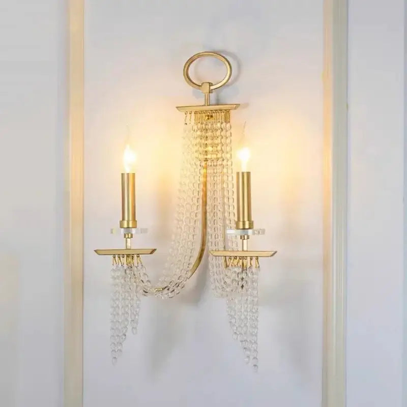 Gold-toned decorbites crystal chandelier wall sconce with two candle-style lights and cascading crystal beads for indoor decor