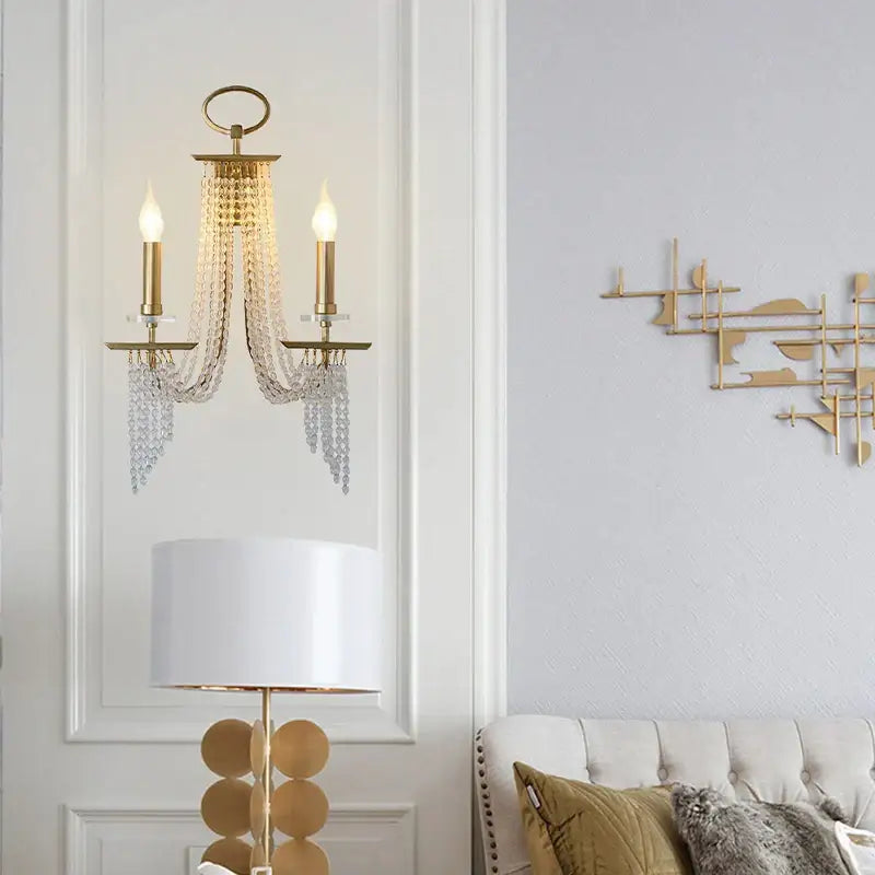 Gold-toned decorbites crystal chandelier wall sconce with two candle-style bulbs and cascading crystal chains for indoor decor