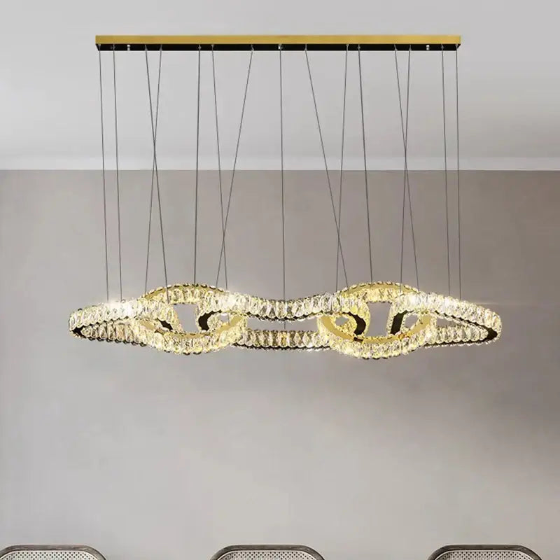 Gold-toned decorbites crystal chandelier with modern flowing ring design suspended by black cords from wooden ceiling mount