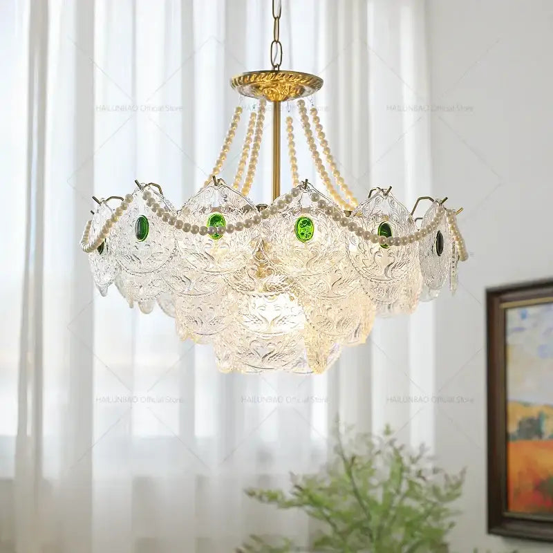 Elegant decorbites crystal chandelier with gold-toned metal, clear glass shades, green gemstones, and cream pearl strands