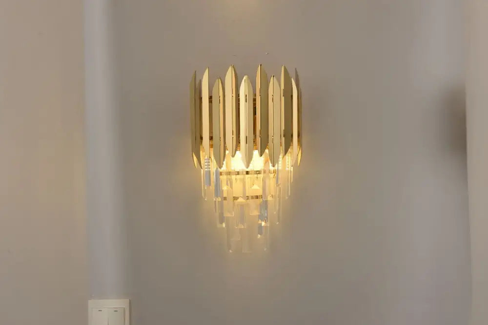 Gold-toned DecorBites crystal chandelier wall sconce with vertical metallic blades and dangling crystal droplets for modern lighting