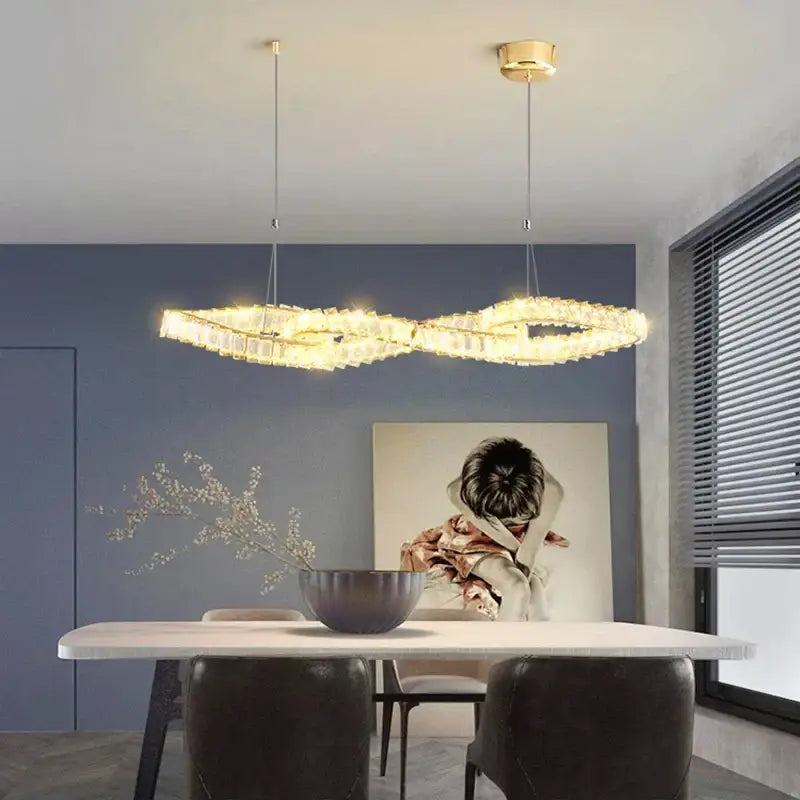 Gold-toned infinity-shaped decorbites crystal chandelier with crystal accents hanging above a dining table