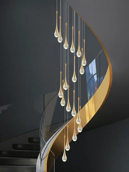 Golden teardrop-shaped decorbites crystal chandelier with crystal accents hanging above curved staircase in living room