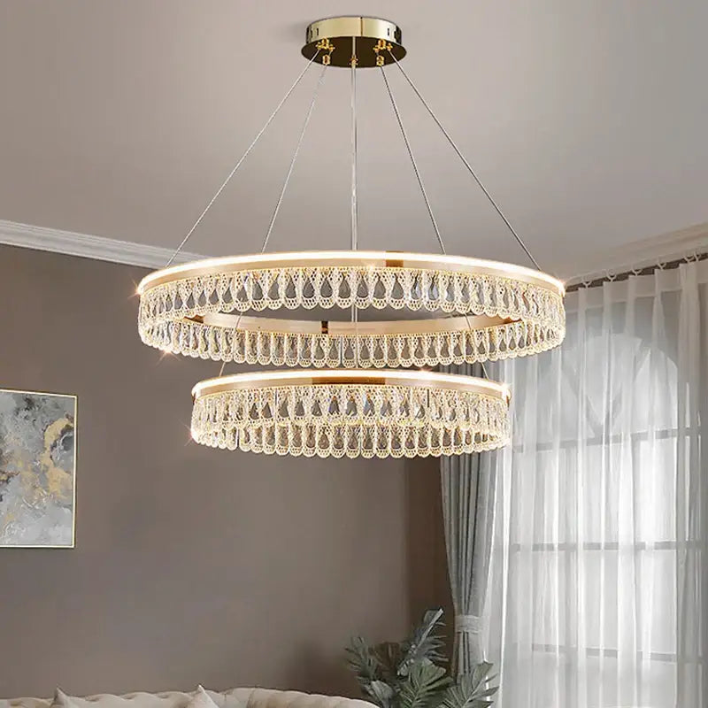 A two-tiered decorbites crystal chandelier with gold-toned mount and dangling crystal droplets for elegant living spaces