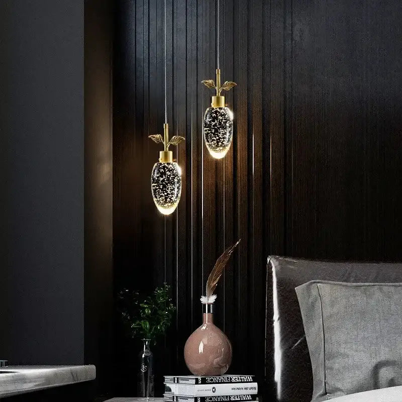 Two gold-toned decorbites crystal chandelier pendant lights with pear-shaped glitter glass shades against dark wood