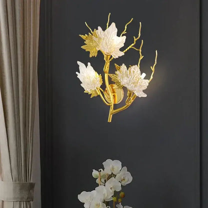 Gold-toned decorbites crystal chandelier wall sconce with white glass flowers and leaf accents on branching stems