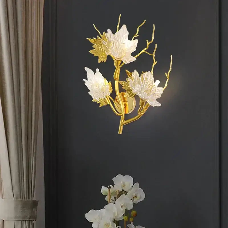 Gold-toned decorbites crystal chandelier wall sconce with white glass flowers and leaf accents on branching stems