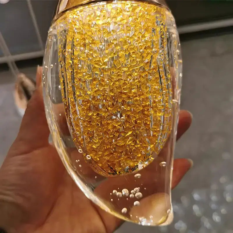 A transparent glass container filled with golden faceted beads and bubbles in decorbites crystal chandelier stair pendant light