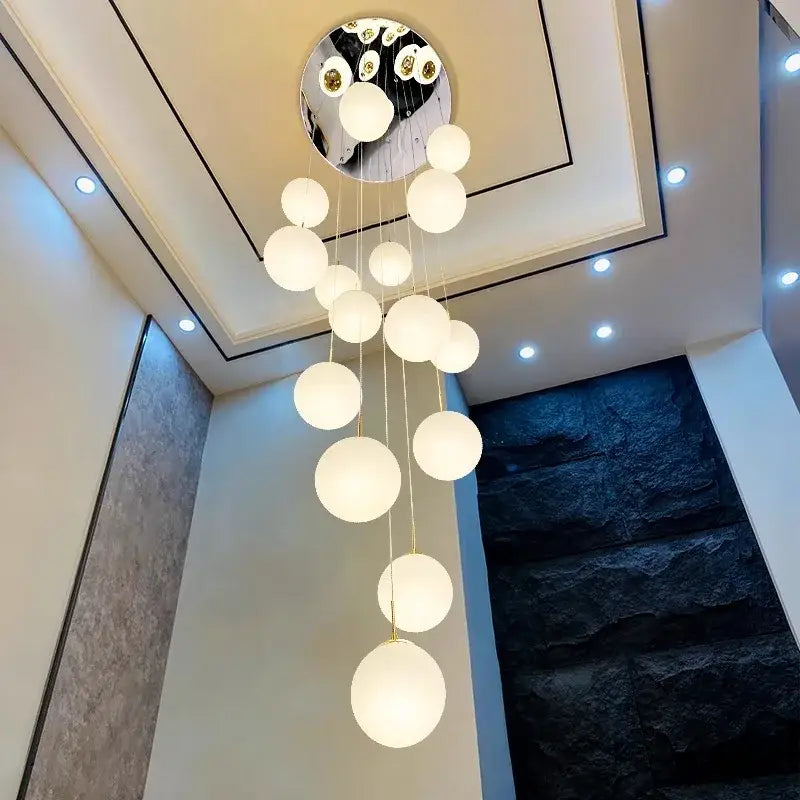 A modern DecorBites crystal chandelier stair pendant light with frosted white globes and mirrored circular base
