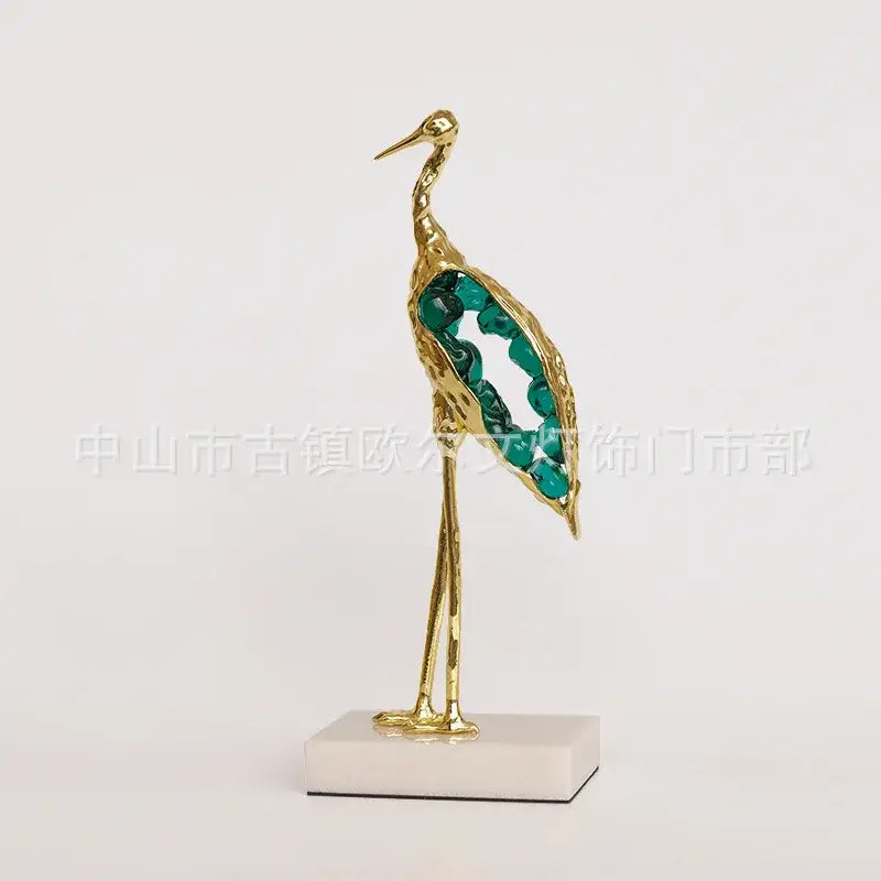 Golden crystal crane sculpture with emerald gemstone accents on wing standing on white marble base decorbites crystal crane