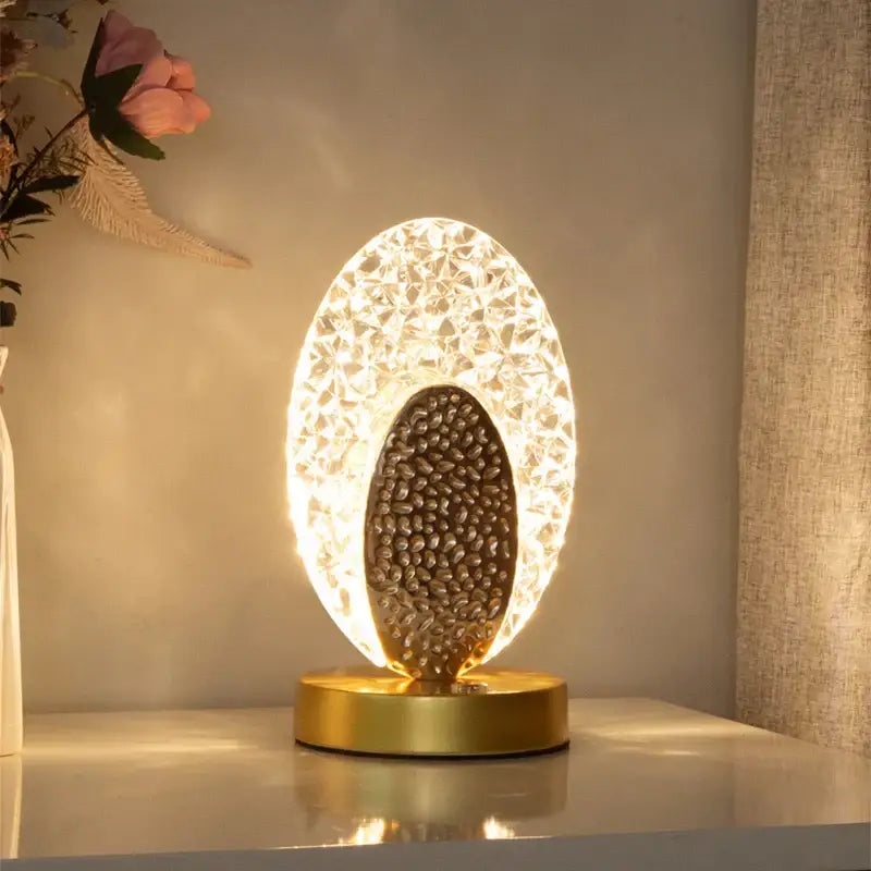Gold-toned decorbites crystal led oval table lamp with faceted crystal shell and dark metallic egg-shaped accent for bedroom