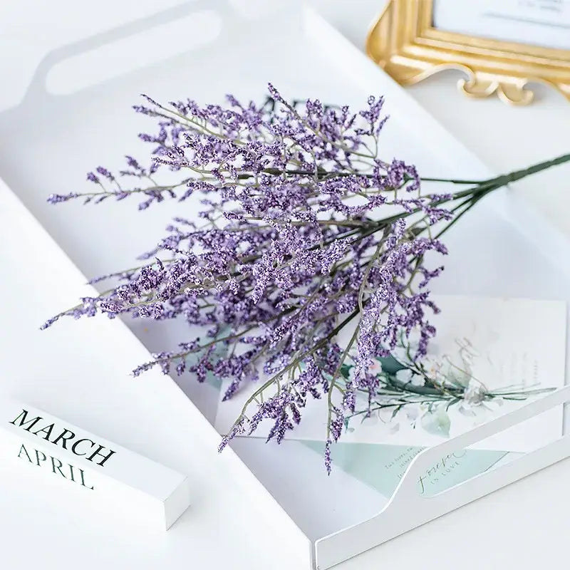 A delicate bouquet of artificial lavender with purple blooms in a modern white tray alongside a mint green ceramic vase with a lemon grass branch for living room decor