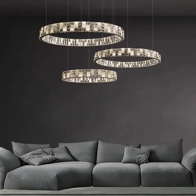 Modern crystal lustre circle chandelier with three tiered circular metallic frames and crystal lustre accents above sofa