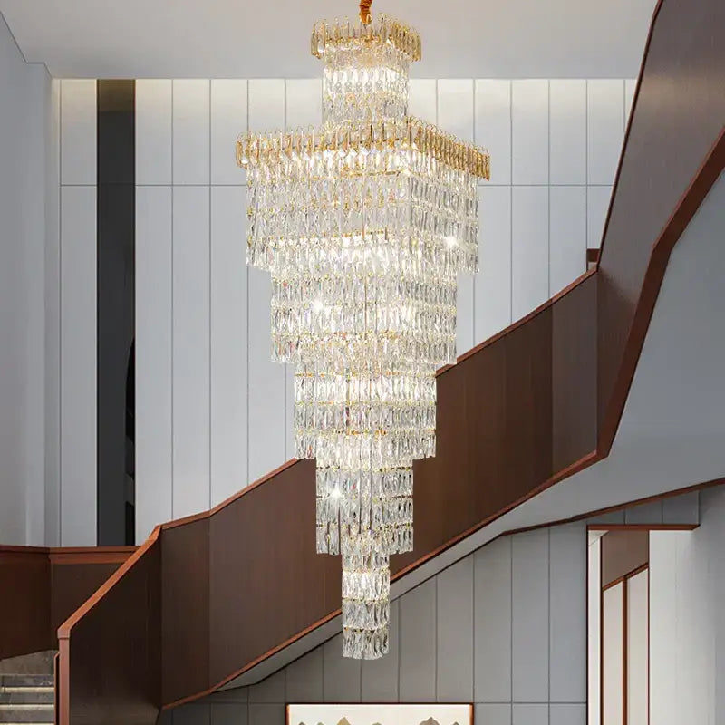 A modern gold crystal luxe living room chandelier with multi-tiered crystal design hangs above a staircase decorbites crystal luxe