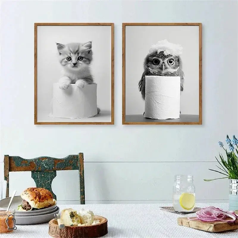 Two framed black-and-white cute animals canvas prints featuring kitten and owl peeking behind toilet paper rolls for bathroom decor