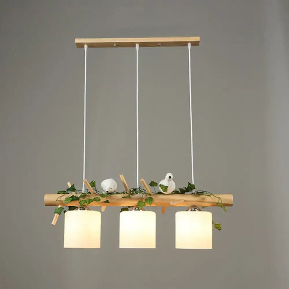 Natural wood pendant light with three cream cylindrical shades and resin bird deco among green ivy for country style restaurants