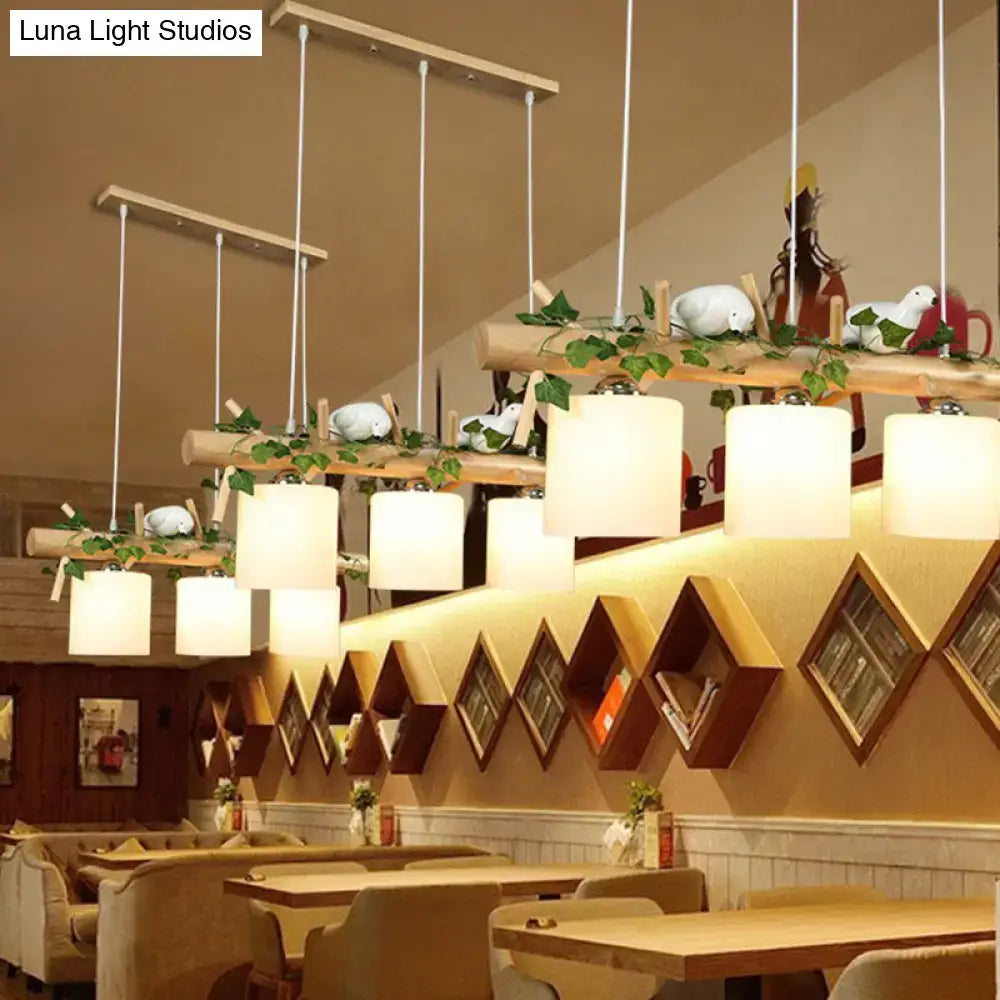 Warm-toned cylindrical milk glass pendant lights with resin bird deco hang from wooden beams with greenery for country style restaurants