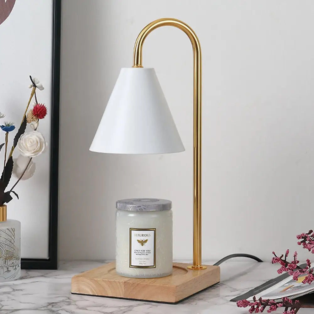Gold-finished decorbites™ dimmable candle warmer lamp with white conical shade and wooden base warming a scented candle jar