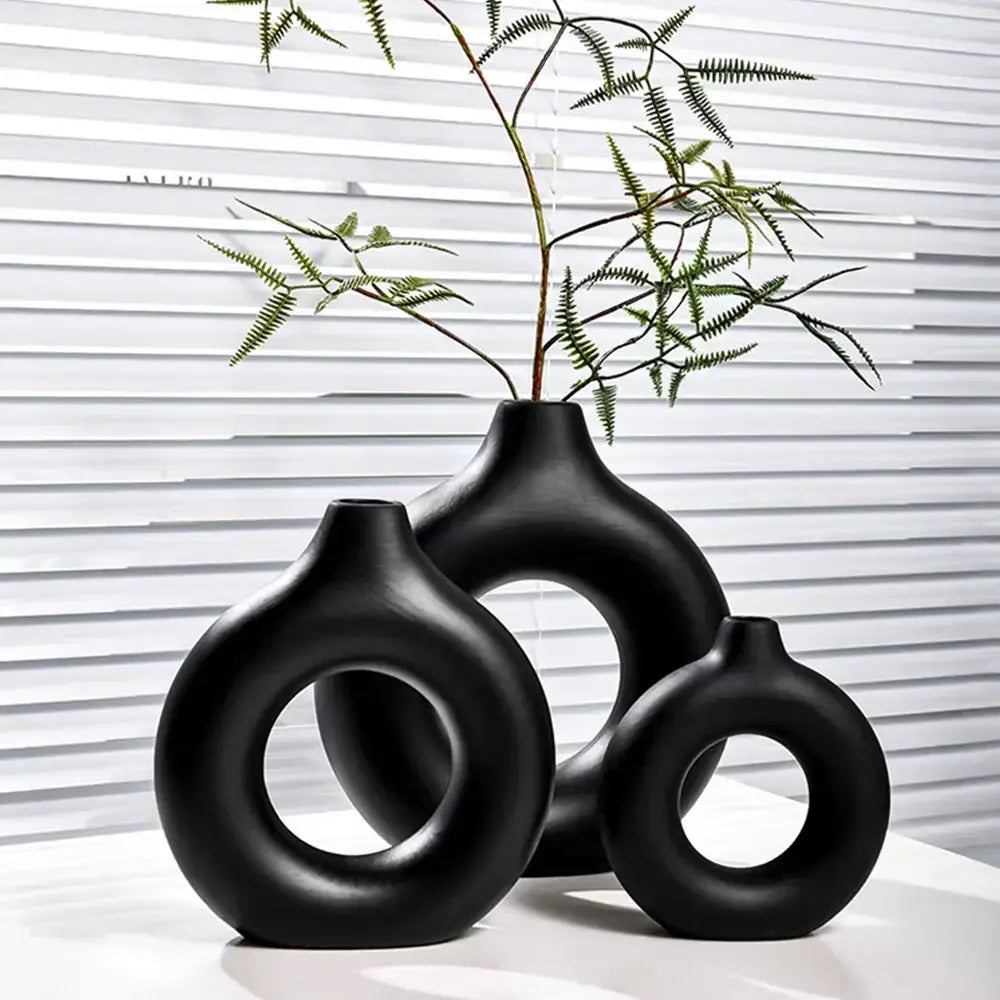 Set of three sleek black ceramic donut shape flower vases with minimalist circular cutouts and matte finish by decorbites