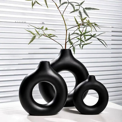 Set of three sleek black ceramic donut shape flower vases with minimalist circular cutouts and matte finish by decorbites