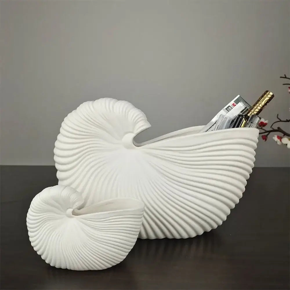 White ceramic vase with shell conch design and ribbed texture holding magazines and a bottle elegant ceramic vase