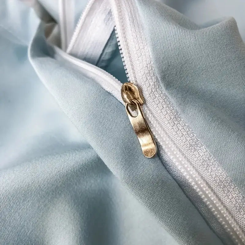 Gold-toned zipper pull on light blue fabric of decorbites elegant embroidery duvet cover with white stitching