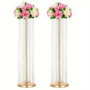 Two tall elegant metal vases with gold finish holding crystal chandeliers and pink white artificial roses for wedding decor