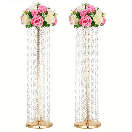 Two tall elegant metal vases with gold finish holding crystal chandeliers and pink white artificial roses for wedding decor