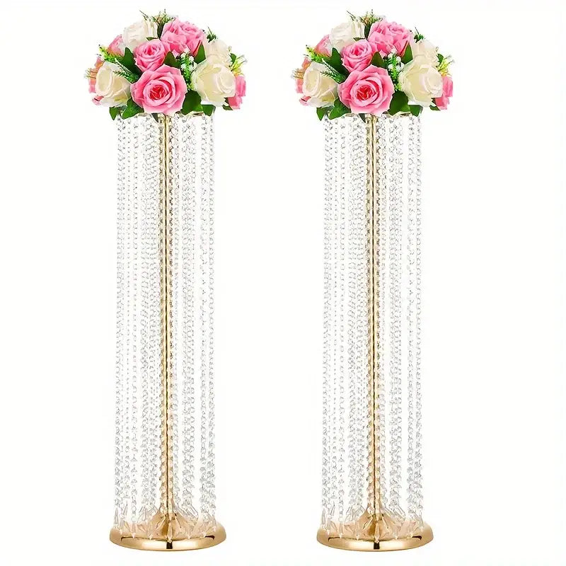 Two tall elegant metal vases with gold finish holding crystal chandeliers and pink white artificial roses for wedding decor