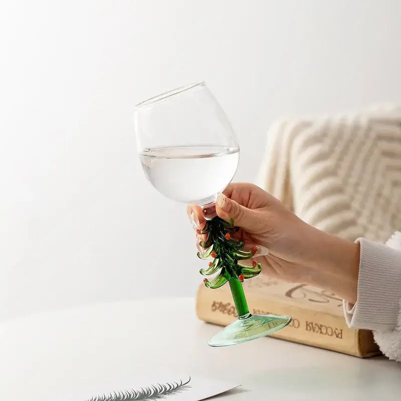 A clear glass wine goblet with a green christmas tree stem decorated with red ornaments from decorbites festive wine glasses