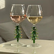 Two festive green glass christmas wine glasses with christmas tree stems and pink ornaments for holiday parties