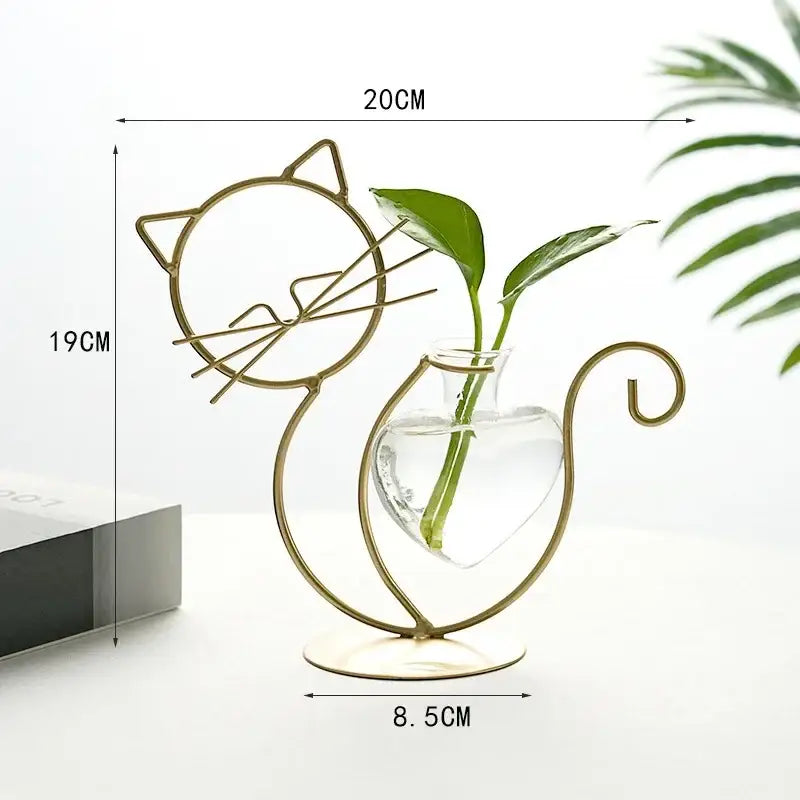Gold metal cat-shaped flamingo metal vase with clear glass heart container holding green plant stems for home decor